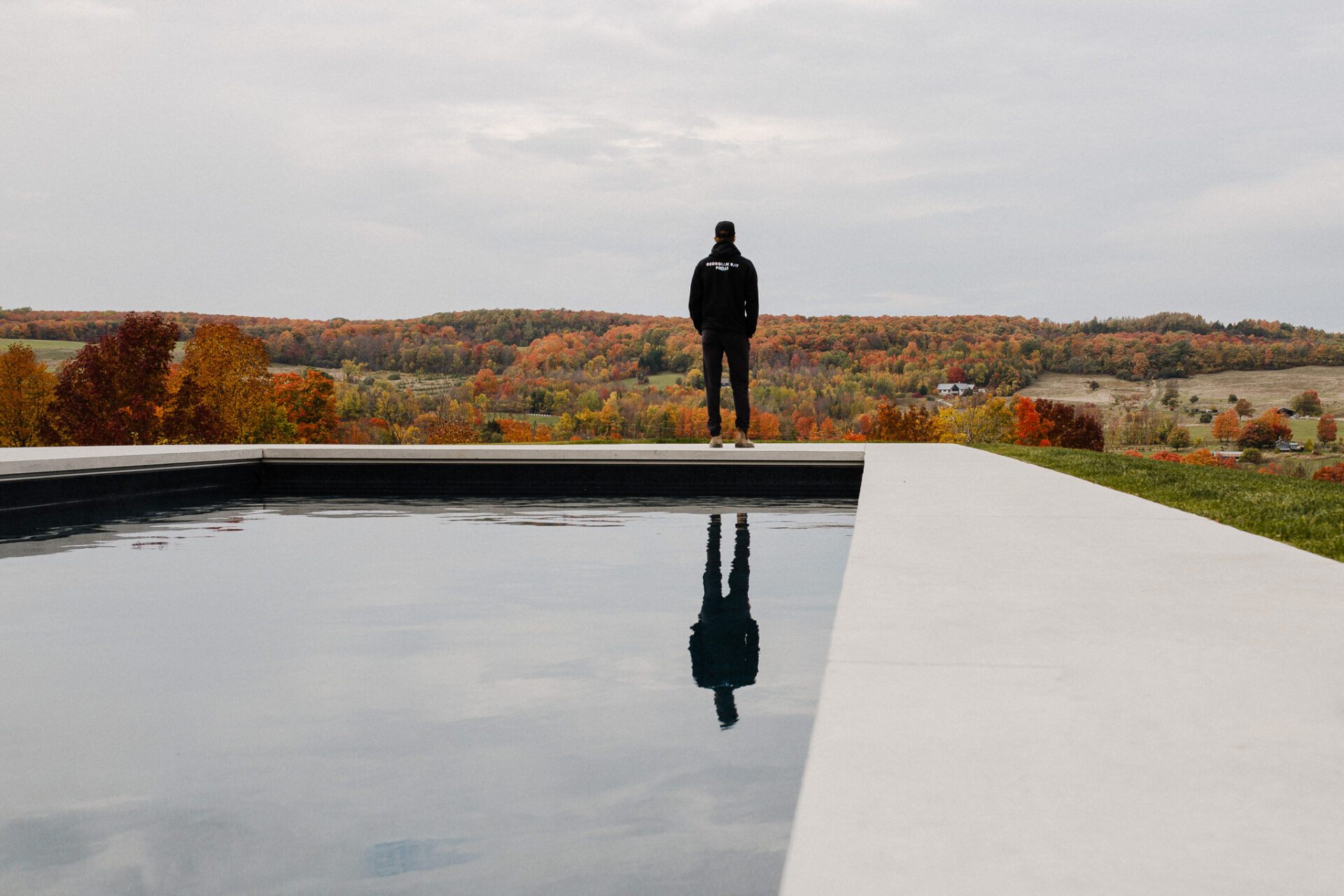 Person standing at the edge of a pool overlooking a scenic autumn landscape.