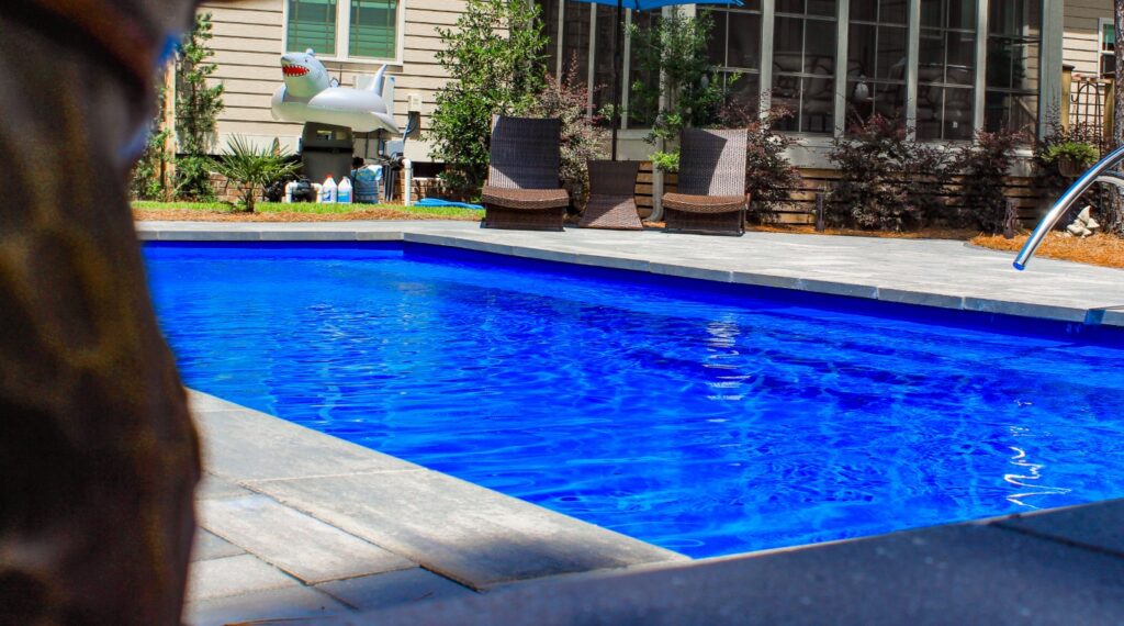 close-up of backyard inground swimming pool with royal blue water, pool loungers in background