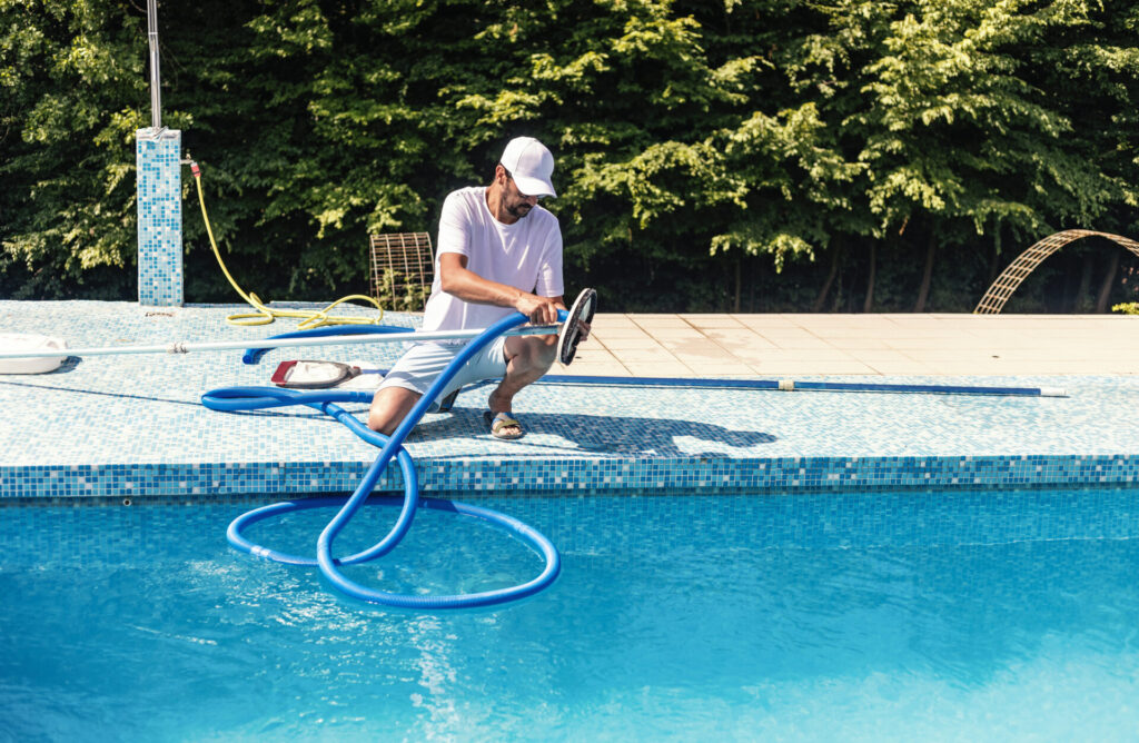 man in white connecting pool hose to attachment to clean swimming pool